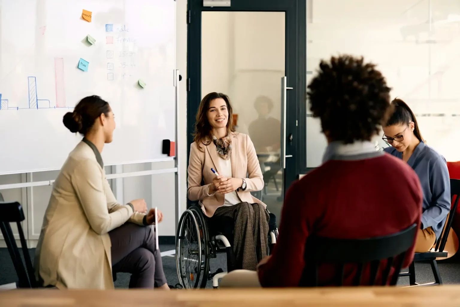 Reunião inclusiva em ambiente de trabalho moderno, com uma mulher em cadeira de rodas participando ativamente da discussão - Assiduidade no trabalho