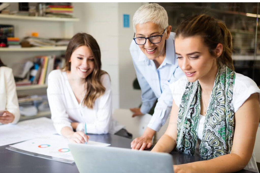 A imagem foca em três mulheres em um ambiente de escritório, que, conforme sugerido pelo nome do arquivo ("diversidade geracional nas empresas"), parecem representar diferentes faixas etárias trabalhando juntas.