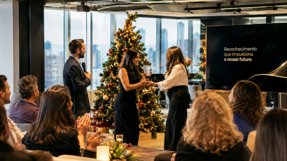 Fotografia realista de uma premiação de fim de ano em uma empresa moderna, realizada em um ambiente corporativo elegante, com amplas janelas de vidro e vista para a cidade. No centro da cena, uma colaboradora recebe um troféu de reconhecimento de outra profissional, enquanto um apresentador segura um microfone e os colegas assistem e aplaudem.