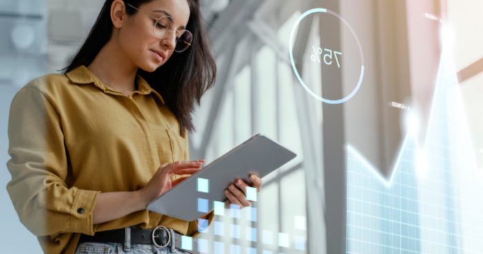 A imagem mostra uma mulher jovem analisando dados em um tablet, em um ambiente moderno e iluminado, com elementos gráficos digitais flutuando ao seu redor.