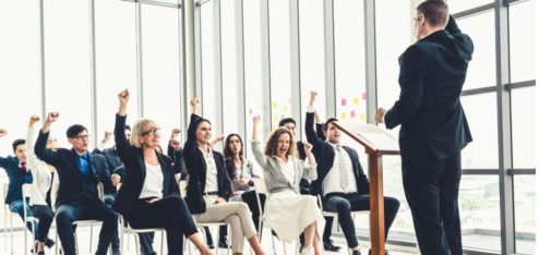 Líder apresenta treinamento para colaboradores em uma conferência corporativa, com equipe reunida