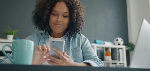 Colaboradora utilizando um smartphone enquanto trabalha em uma mesa de escritório, representando o uso de soluções digitais para gestão de benefícios, comunicação e praticidade no ambiente corporativo.