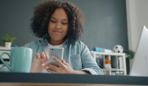 Colaboradora utilizando um smartphone enquanto trabalha em uma mesa de escritório, representando o uso de soluções digitais para gestão de benefícios, comunicação e praticidade no ambiente corporativo.