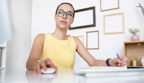 Mulher de óculos trabalhando no computador e fazendo anotações, representando dúvidas sobre banco de horas negativo nova lei.