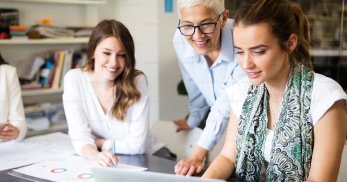 A imagem foca em três mulheres em um ambiente de escritório, que, conforme sugerido pelo nome do arquivo ("diversidade geracional nas empresas"), parecem representar diferentes faixas etárias trabalhando juntas.