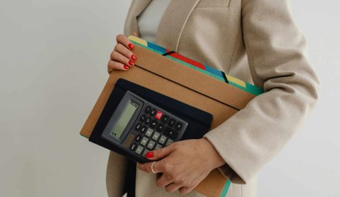 Mulher segurando uma calculadora e pastas organizadas, representando a importância da organização no trabalho e o uso de ferramentas adequadas para produtividade.