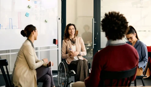 Reunião inclusiva em ambiente de trabalho moderno, com uma mulher em cadeira de rodas participando ativamente da discussão - Assiduidade no trabalho