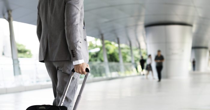 Imagem de um homem vestido de terno com uma mala em um aeroporto